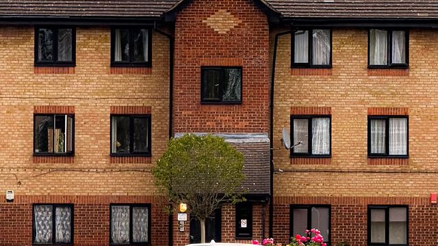 A brick block of flats behind a low hedge of roses